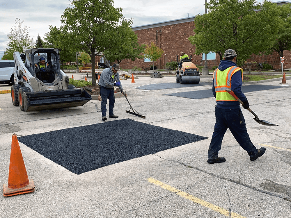 Infrared asphalt heater warming a section of residential driveway while a worker prepares to rake it